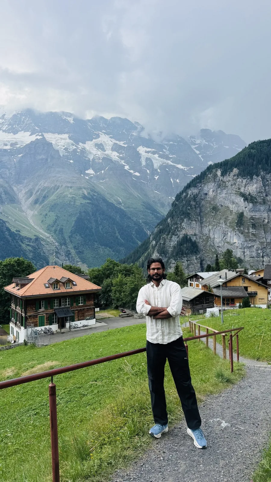 Gautam Kumawat at a railing above a green alpine valley, a chalet below and cloud sitting on the peaks